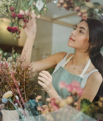 A woman carefully arranges colorful flowers in a vibrant flower shop, showcasing her floral design skills.