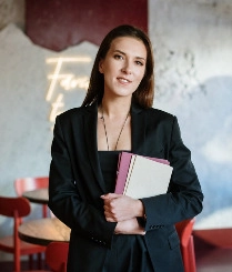 A woman in a suit stands confidently, holding a book in her hands, ready to share her knowledge.