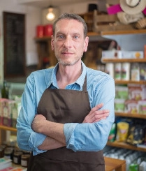 A man stands with arms crossed in front of a store, looking confidently at the camera.